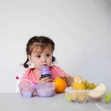 A smiling baby surrounded by colorful fruits and vegetables, representing the nutritious diet required for a baby's growth from 6 to 12 months.