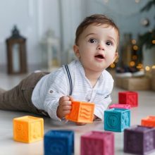 A 9-month-old baby joyfully playing with colorful blocks, promoting motor skills development and hand-eye coordination.