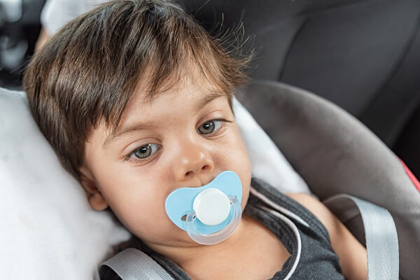 Child holding a pacifier while parent gently removes it from their mouth.