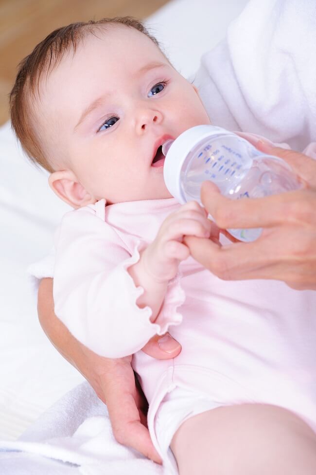 A mother holding a baby bottle while feeding her infant.