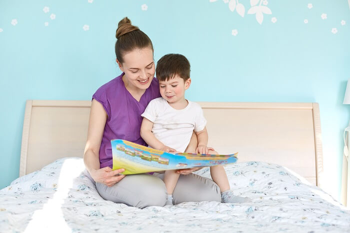 A parent sitting on a chair, reading a bedtime story to a baby lying in a crib.