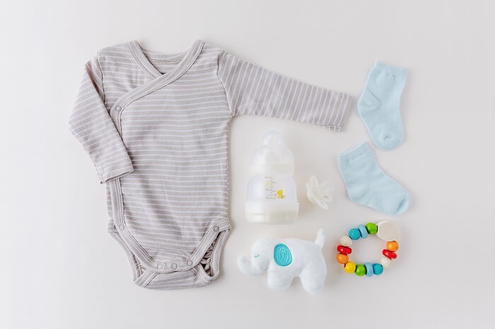 A collage of essential baby products including a crib, stroller, diaper bag, baby monitor, onesies, baby bottles, and a pacifier.