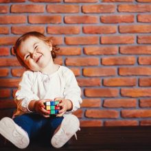 A joyful baby sitting on the floor, surrounded by colorful building blocks, with a big smile while babbling happily.