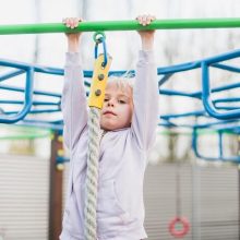 A smiling baby engaging with a pull-up bar, supported by parents, highlighting the developmental advantages of this activity.