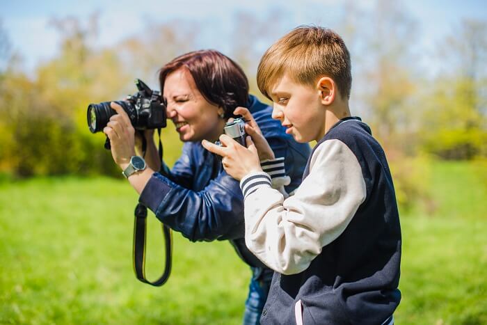 A caring sports mom and her happy baby boy using a high-quality camera outdoors, emphasizing safety and photography.
