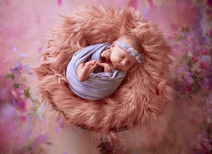 A serene newborn baby sleeps soundly in the arms of a skilled photographer, bathed in soft, natural light in a cozy studio setting. The photographer delicately captures tiny fingers and toes, illustrating the art of newborn photography.